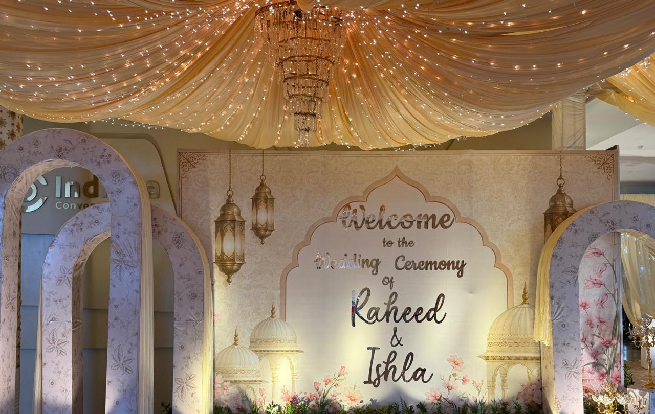 Wedding welcome backdrop beneath a draped champagne ceiling with fairy lights and a crystal chandelier